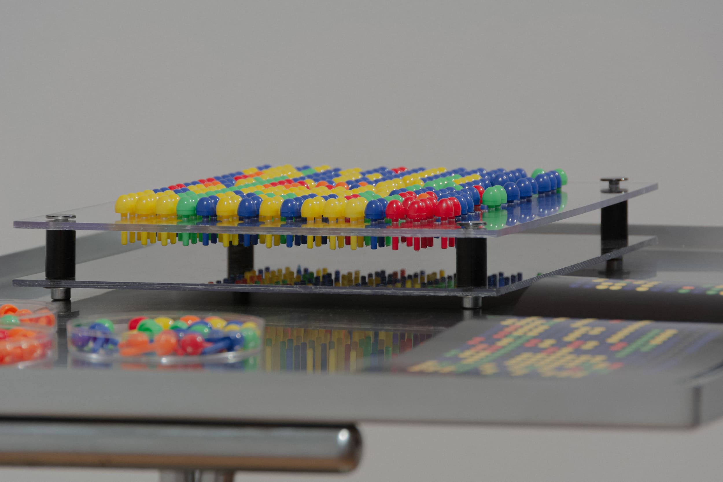 A colorful puzzle toy displays a matrix array of small, dome-shaped details in red, yellow, green, and blue, creating a vibrant pattern. A clear, modern design on a sleek, reflective surface conveys a sense of playfulness.