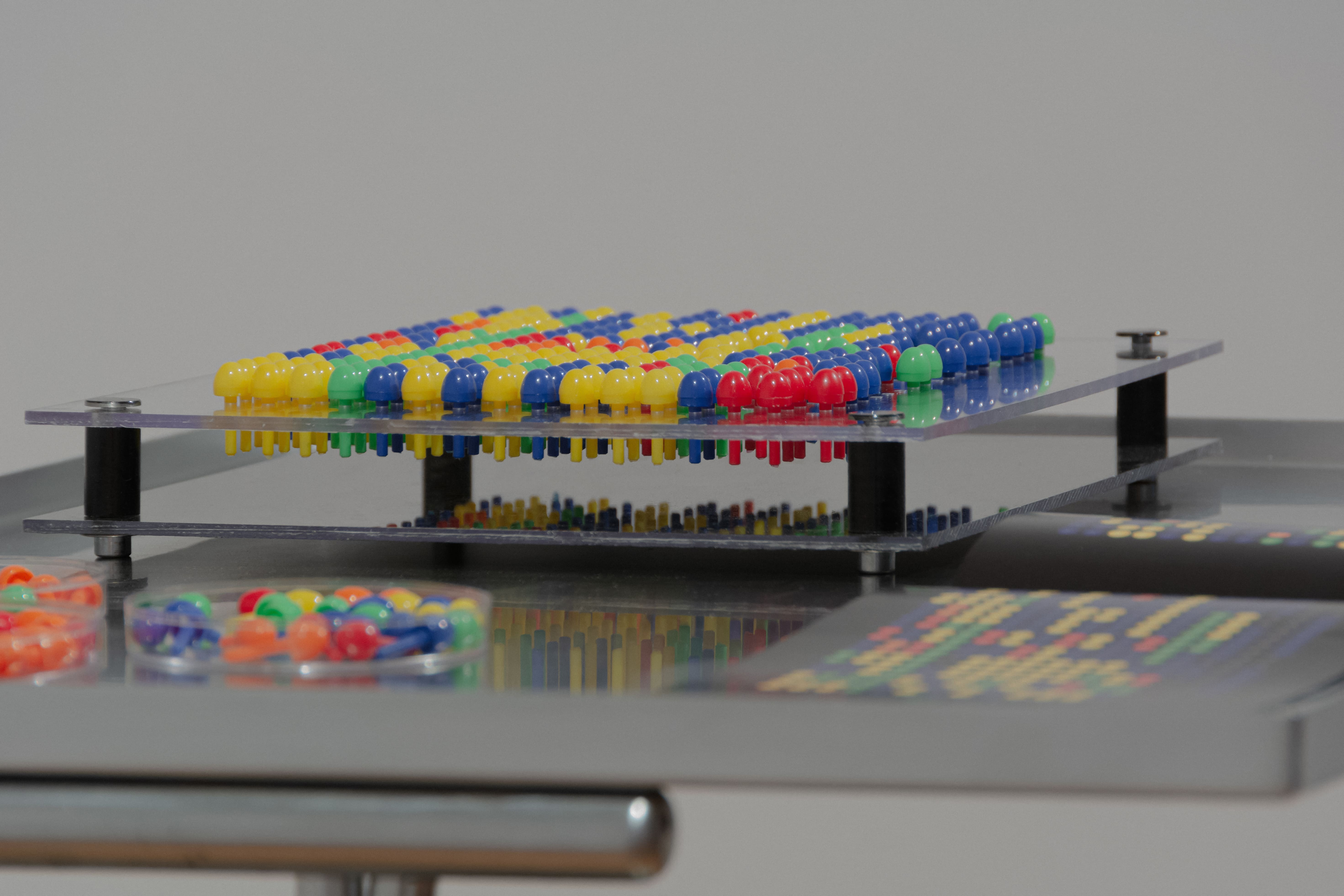 A colorful puzzle toy displays a matrix array of small, dome-shaped details in red, yellow, green, and blue, creating a vibrant pattern. A clear, modern design on a sleek, reflective surface conveys a sense of playfulness.