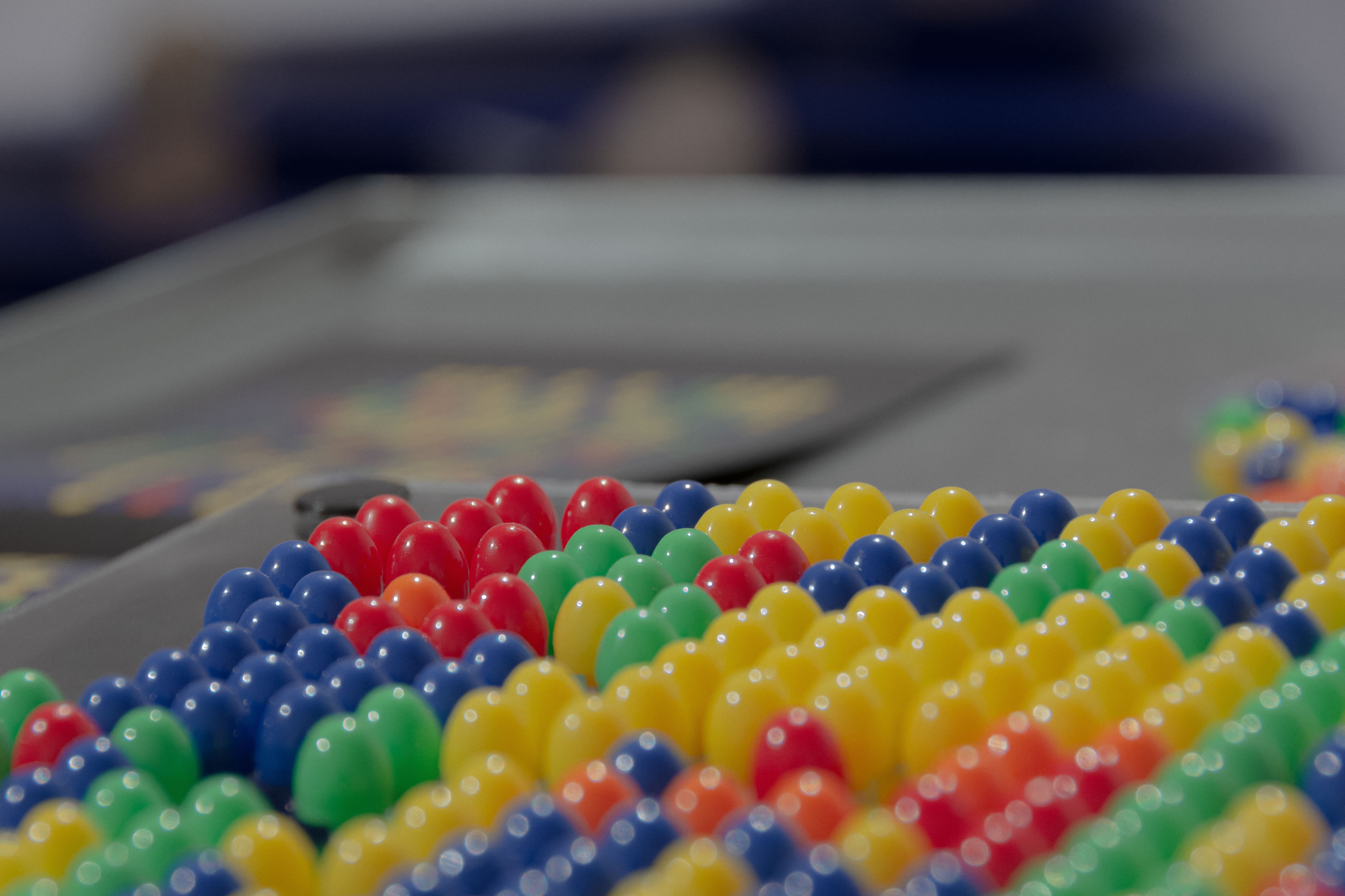 Rows of colorful plastic pegs, including red, green, yellow, and blue, arranged on a flat surface. Background blurred, conveying a playful atmosphere.