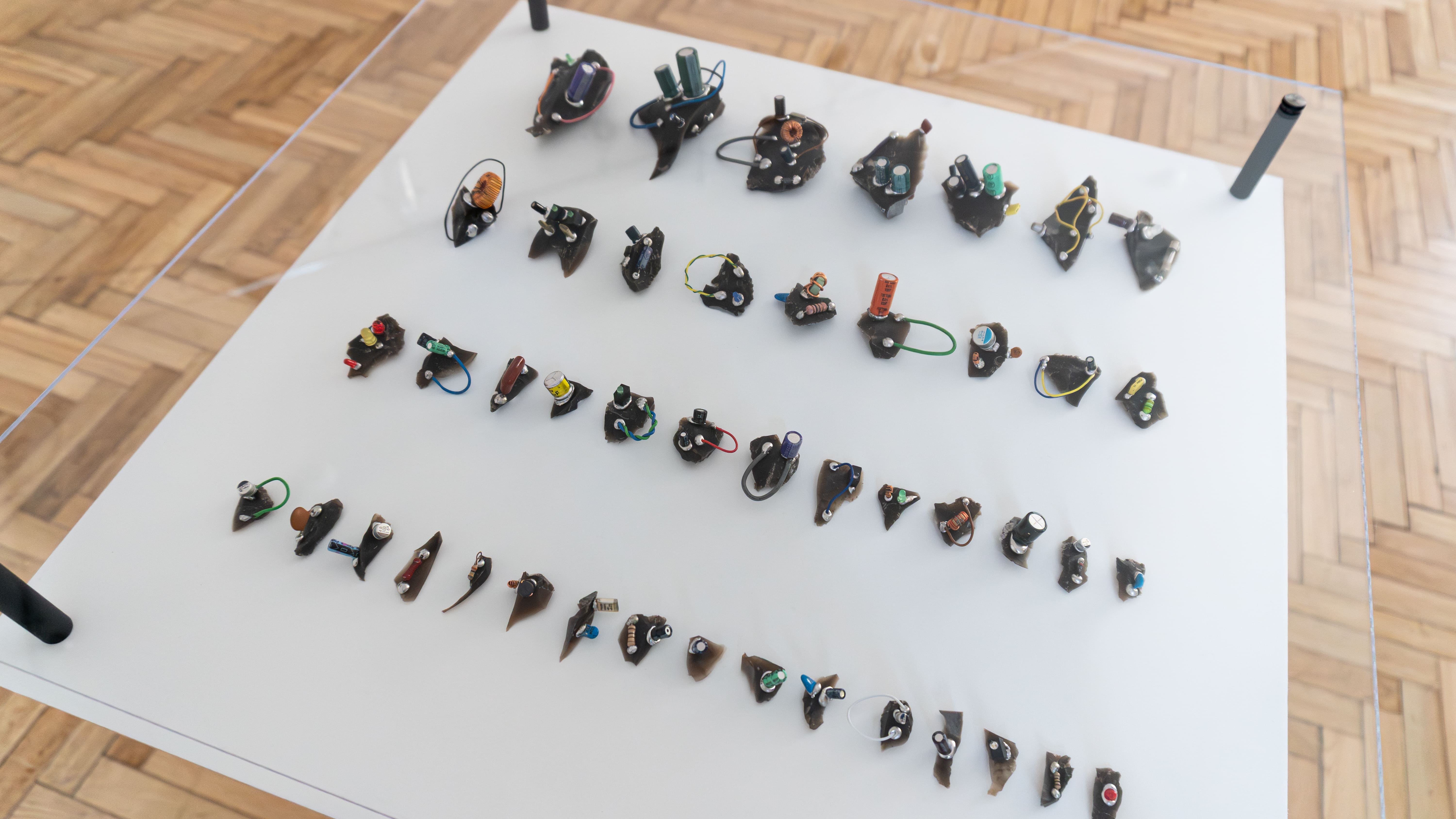 Array of small, abstract sculptures resembling circuit boards, with colorful wires and components, neatly aligned on a white background.