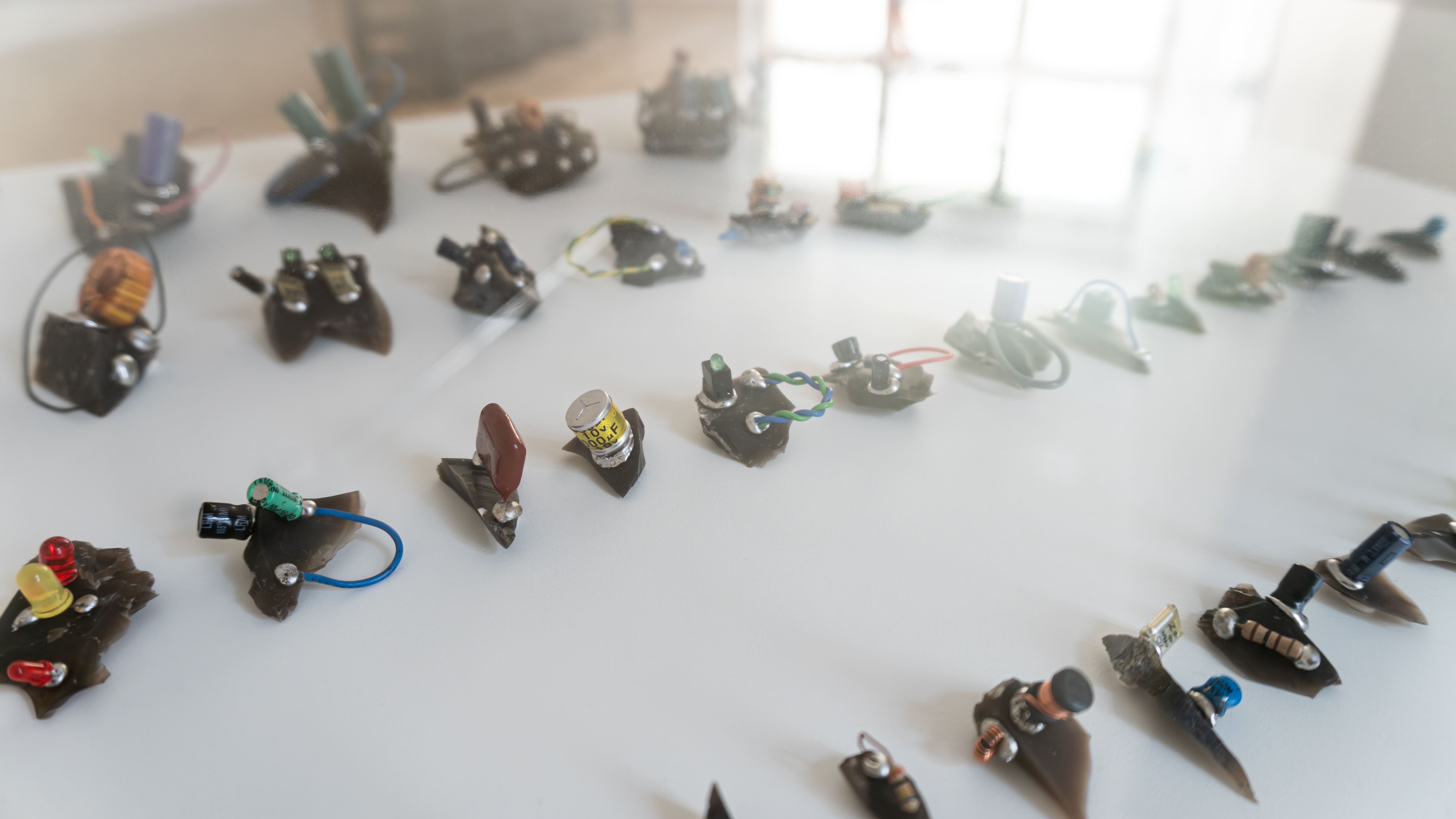 A collection of small electronic sculptures made from wires, capacitors, and resistors are displayed on a white surface, reflecting creativity and innovation.